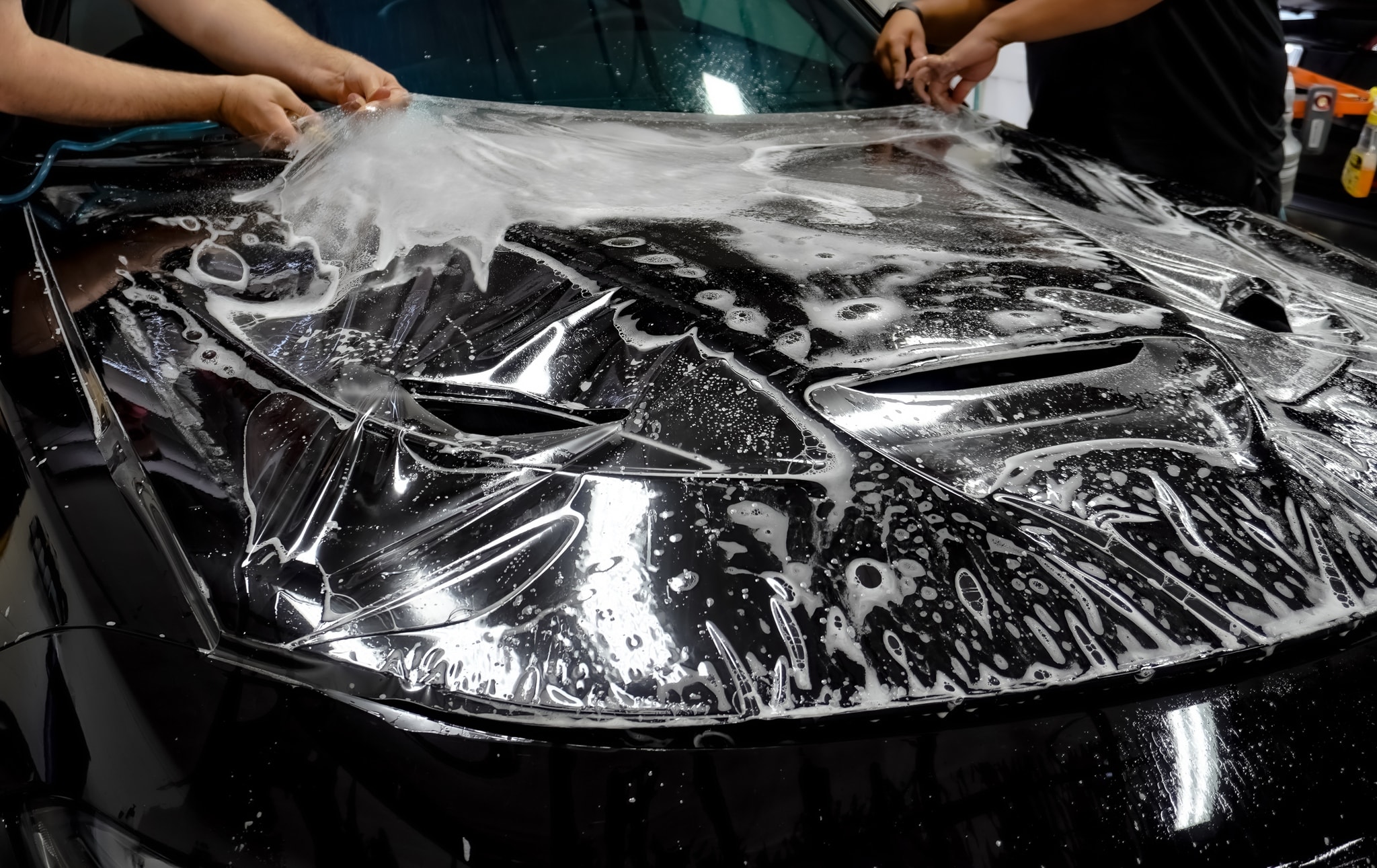 Technician applying clear paint protection film to a car hood